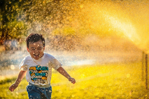 A joyful child playing in water sprinklers during a sunny day.