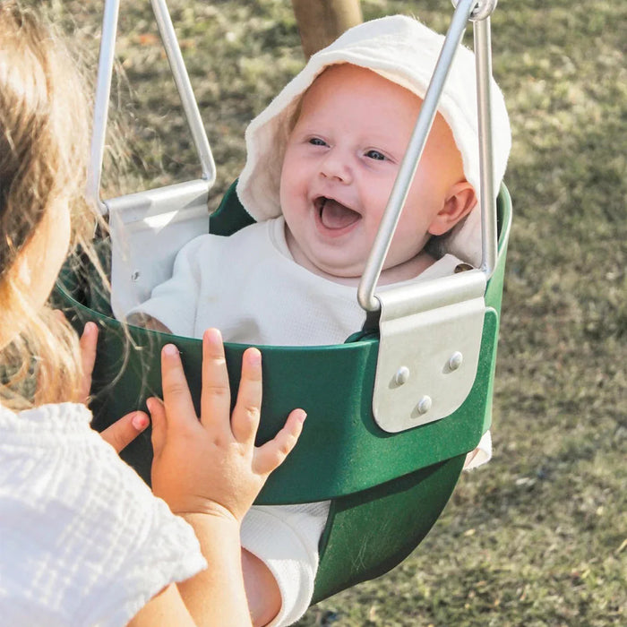 Baby in a green swing with a smiling expression, outdoors.