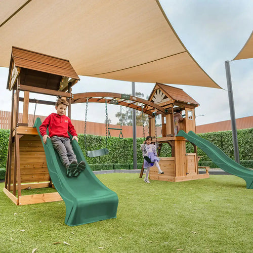 Wooden playground structure with green slides and shade sails overhead.