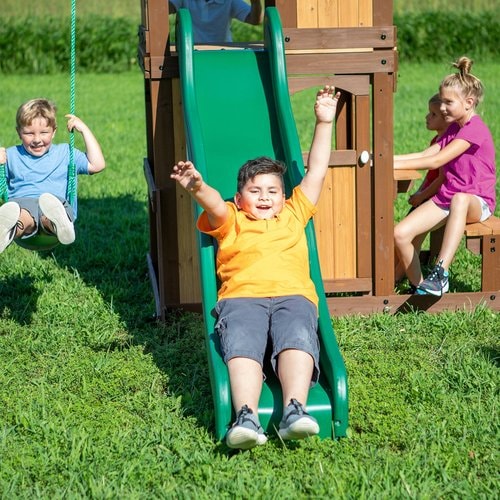 Close up image of a little boy swinging on the swing, a little boy sliding on the green slide and two little girls sitting in front of the snack bar of Lakewood Swing And Play Set