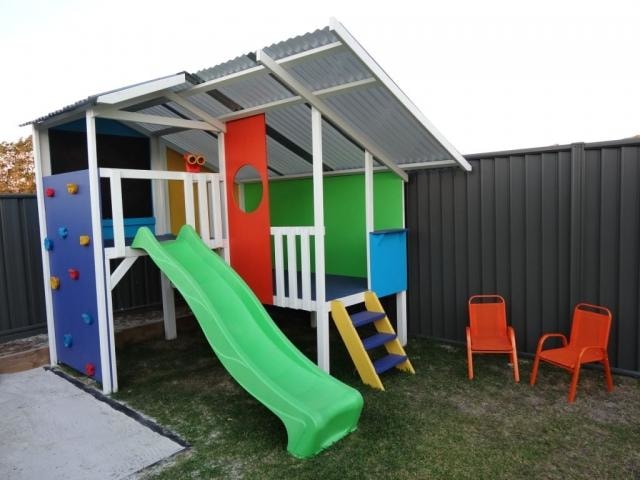 Mega Triplex Cubby House - colourful design with rock wall, orange chairs and green slide