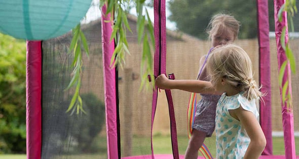 Close up image of 4.5ft Junior Kids Trampoline Pink toddler trampoline with 2 little girls, one standing inside the trampoline and one at the entrance of the trampoline