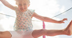 Blurred image of 4.5ft Junior Kids Trampoline Pink as the background and a close up image of a little girl jumping on the toddler trampoline