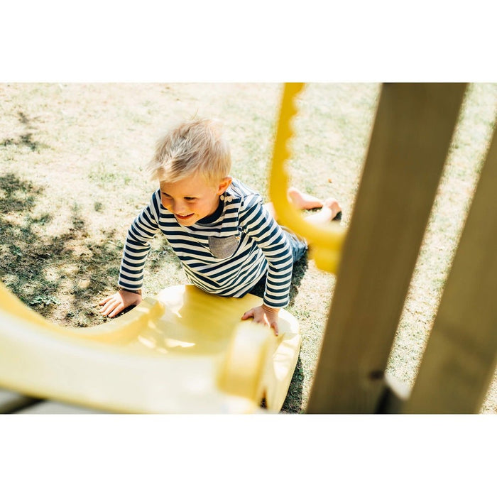 Close up image of a little boy sliding from the yellow slide of the Toddler Tower Outdoor Playset